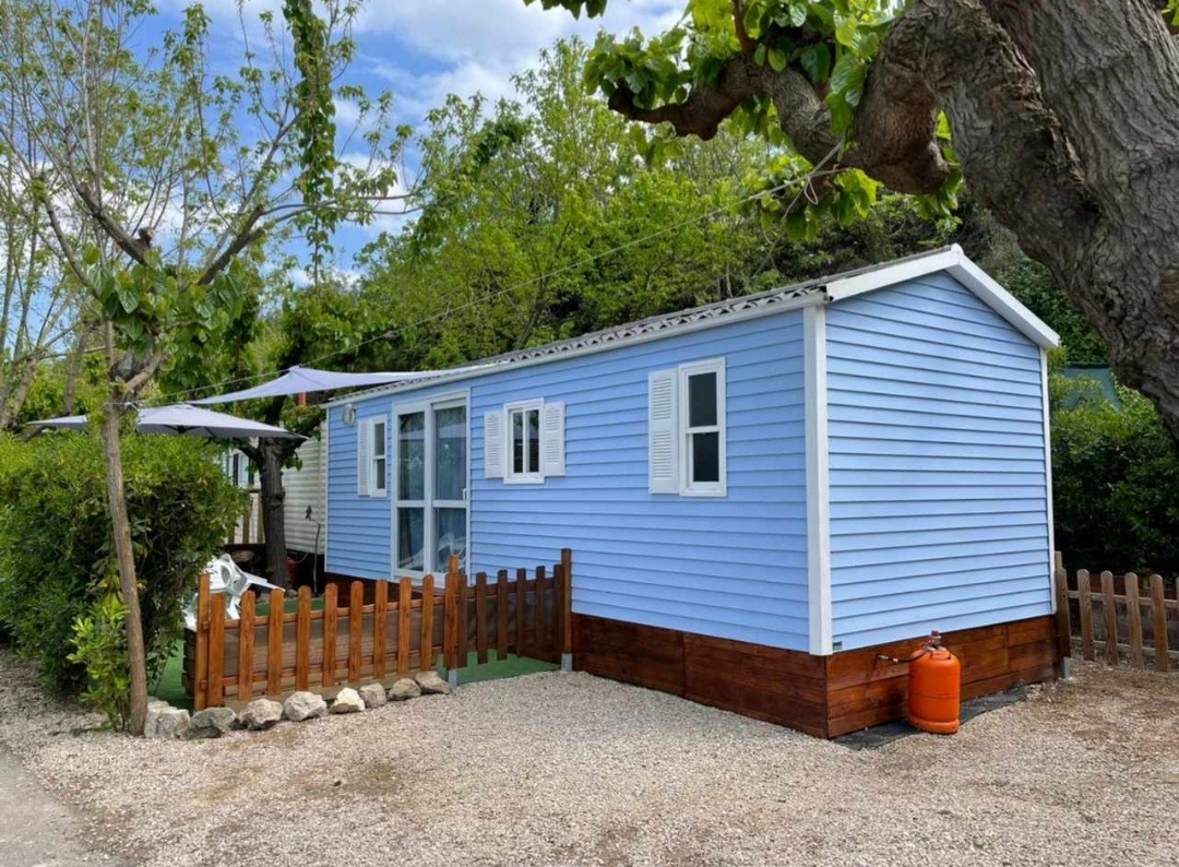 Mobile home azul con valla de madera y terraza